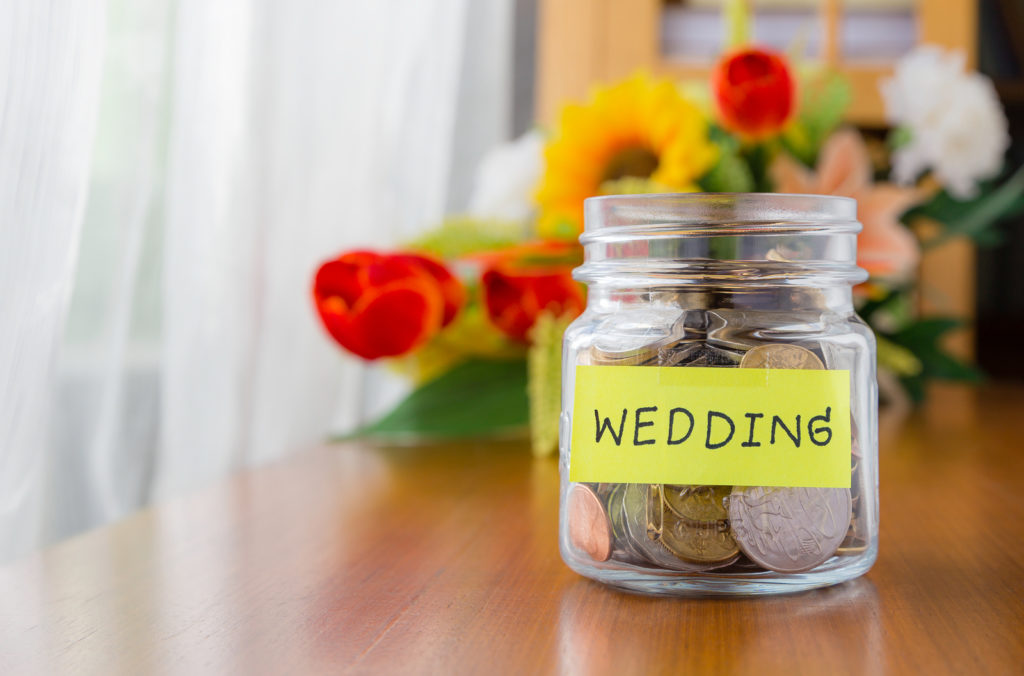 Many world coins in a money jar with wedding label on jar beautiful flowers on background